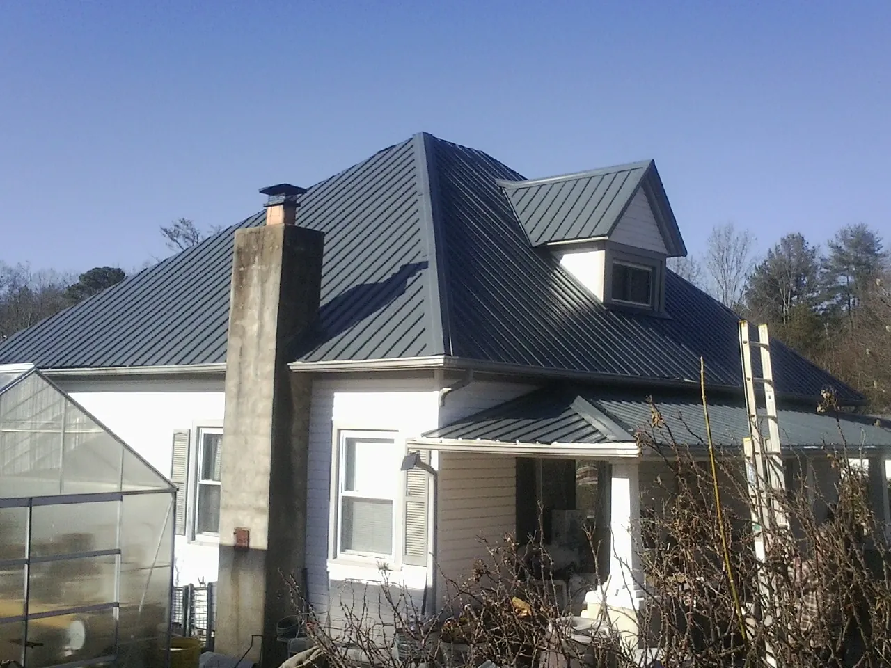 Dark blue standing seam metal roof on a white farmhouse with dormer — Slate & Tile Roof Repair by Roofing Brothers in Pleasantville
